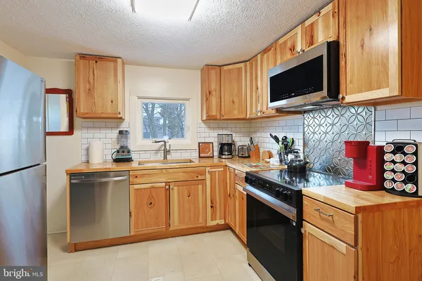 a kitchen with stainless steel appliances granite countertop a stove top oven a sink dishwasher and a refrigerator with wooden cabinets