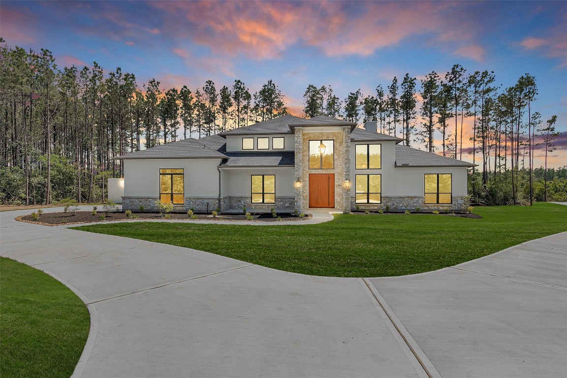 Set on over 4.5 wooded acres, this newly built estate with guest house features a striking stucco and stone exterior with soaring windows and a bold wood-accented entry.