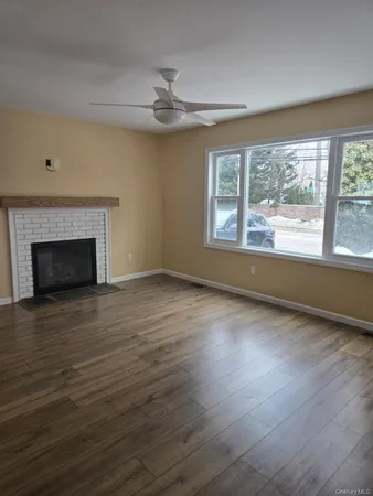 a view of an empty room with wooden floor fireplace and a window