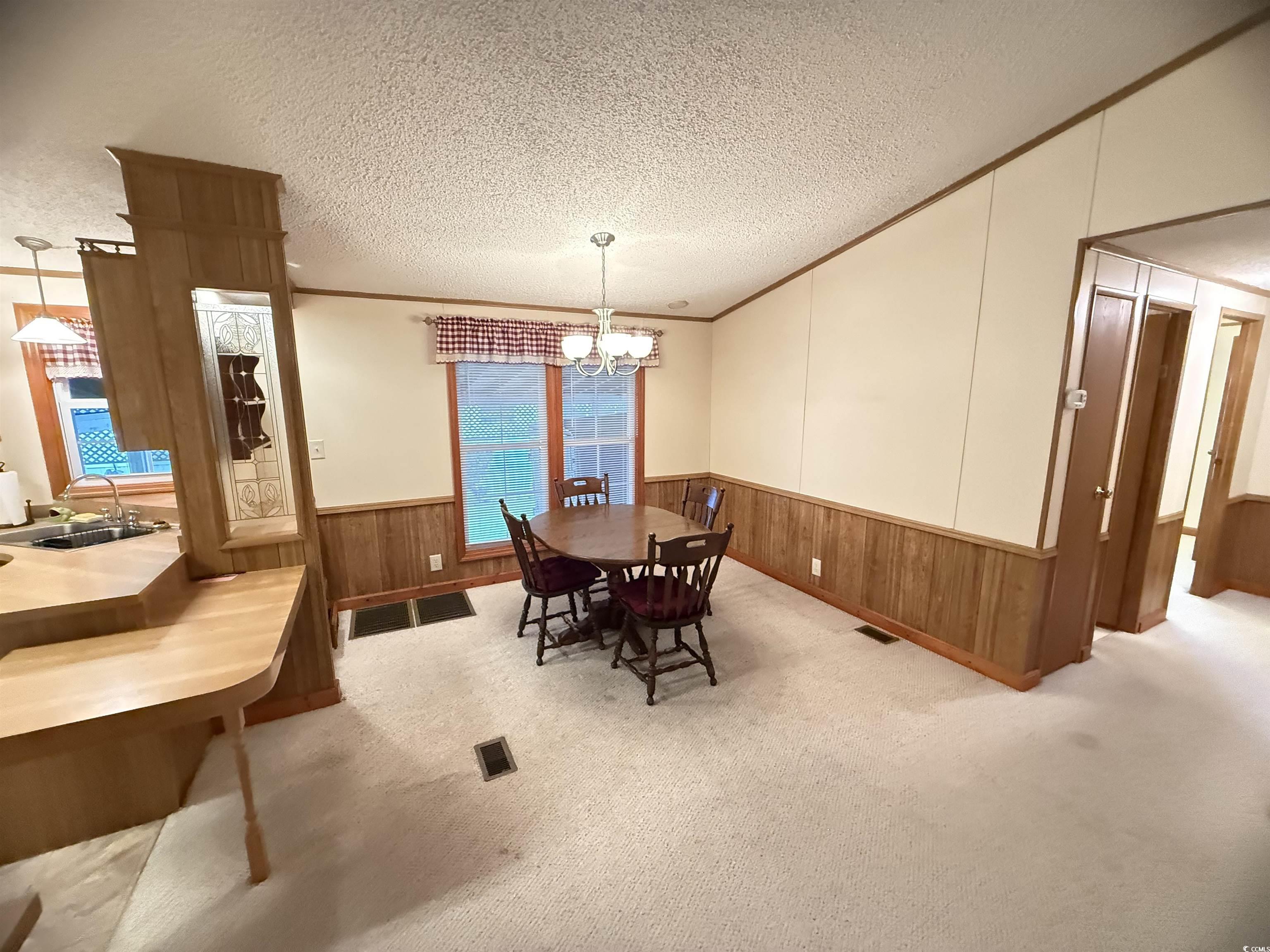 8 Buccaneer Street Murrells Inlet, SC 29576 - Photo 11 of 28 Dining space featuring carpet, crown molding, a textured ceiling, wood walls, and a chandelier
