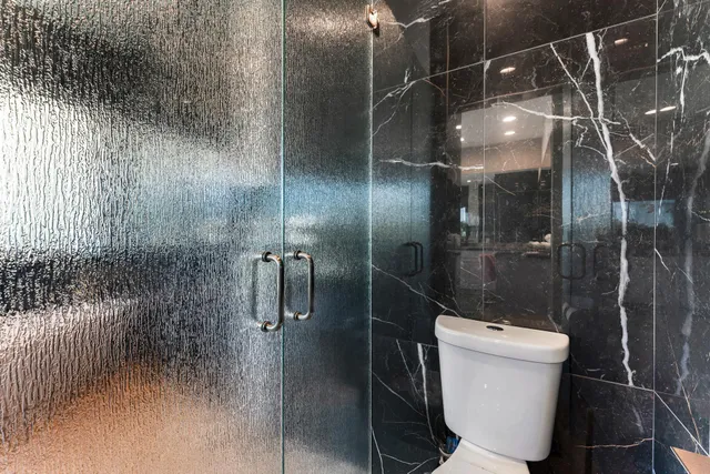 a bathroom with a granite countertop sink a toilet a mirror and shower