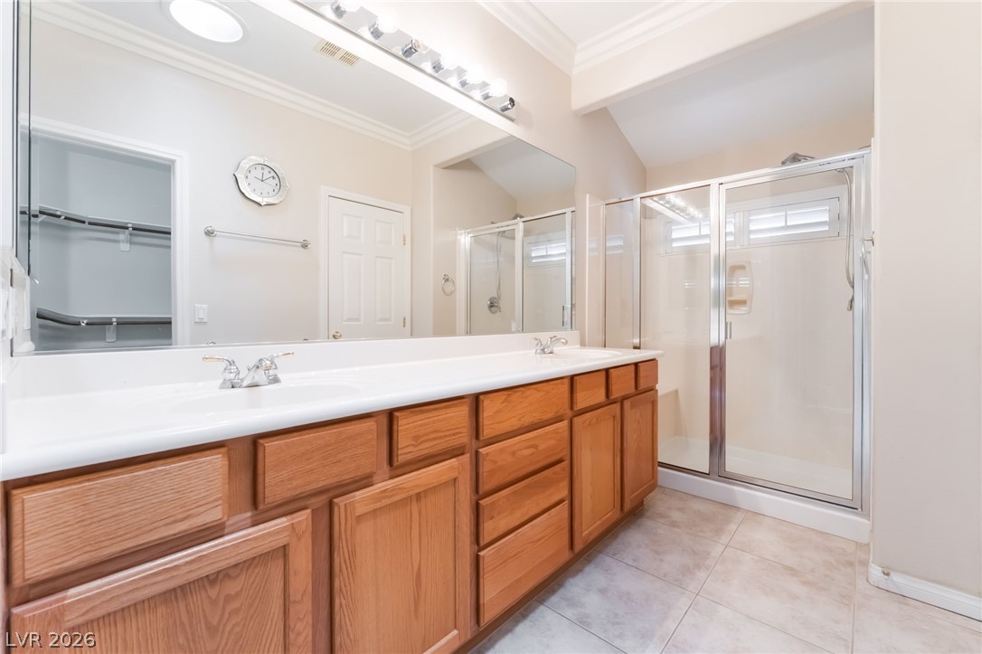 10481 Riverside Park Avenue Las Vegas, NV 89135 - Photo 21 of 51 Bathroom featuring double vanity, a stall shower, crown molding, a walk in closet, and light tile patterned flooring