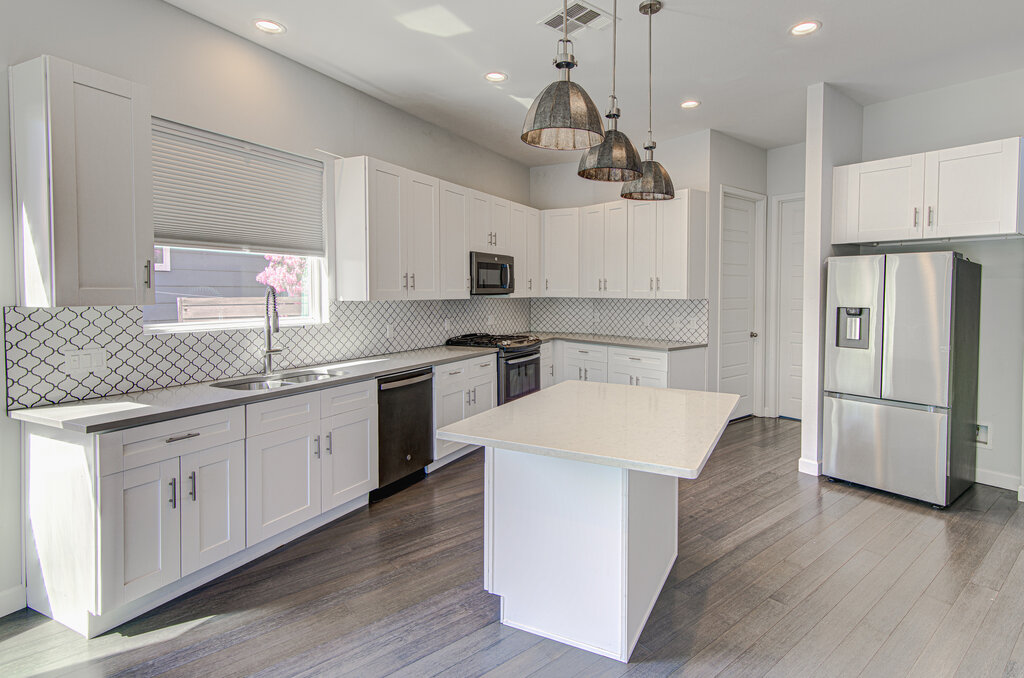 2406 East 16th Street Austin, TX 78702 - Photo 17 of 39 a kitchen with stainless steel appliances kitchen island a refrigerator a sink dishwasher a stove and white cabinets with wooden floor