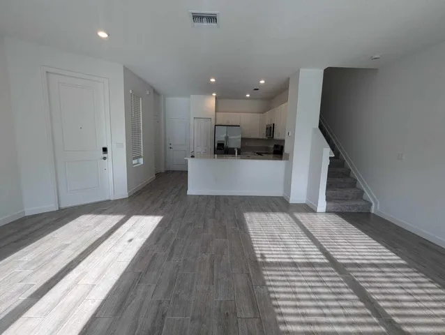 a view of a living room with kitchen island wooden floor and staircase