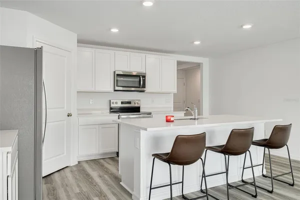 a kitchen with stainless steel appliances a stove a refrigerator and a dining table with wooden floor