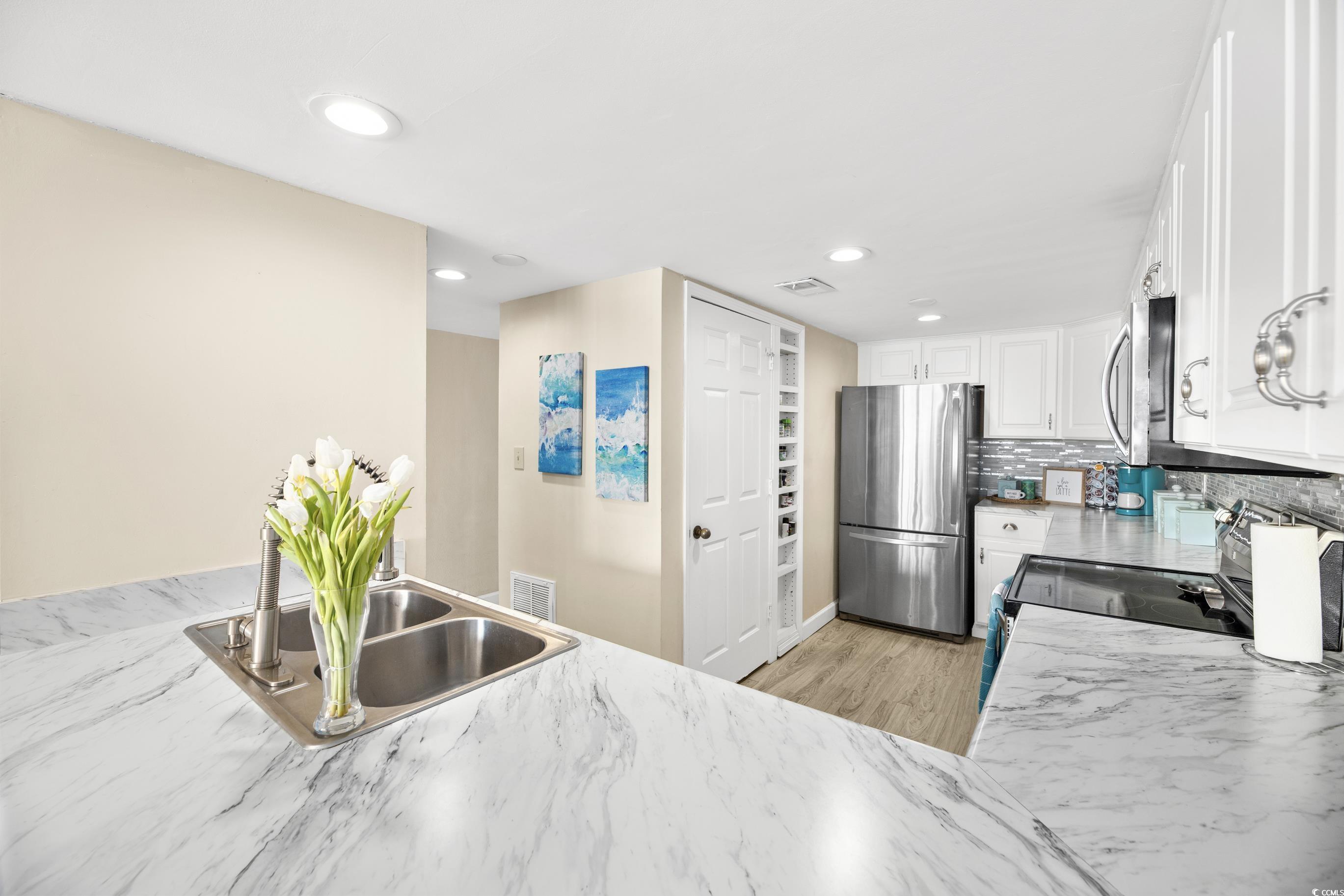 1108 North Waccamaw Drive, Unit 304 Murrells Inlet, SC 29576 - Photo 8 of 34 Kitchen featuring appliances with stainless steel finishes, white cabinetry, light wood-type flooring, tasteful backsplash, and recessed lighting