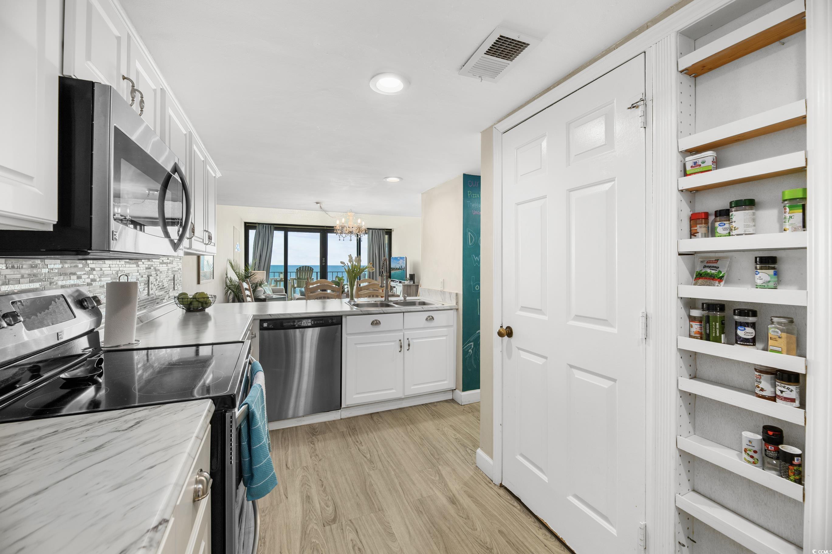 1108 North Waccamaw Drive, Unit 304 Murrells Inlet, SC 29576 - Photo 10 of 34 Kitchen featuring stainless steel appliances, white cabinetry, light wood-type flooring, light countertops, and a chandelier