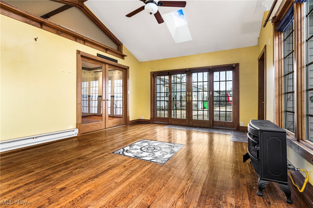 4870 15th Street Southwest Canton, OH 44710 - Photo 13 of 36 Sun room featuring a wood stove, baseboard heating, a skylight, a ceiling fan, high vaulted ceiling, and an abundance of natural light