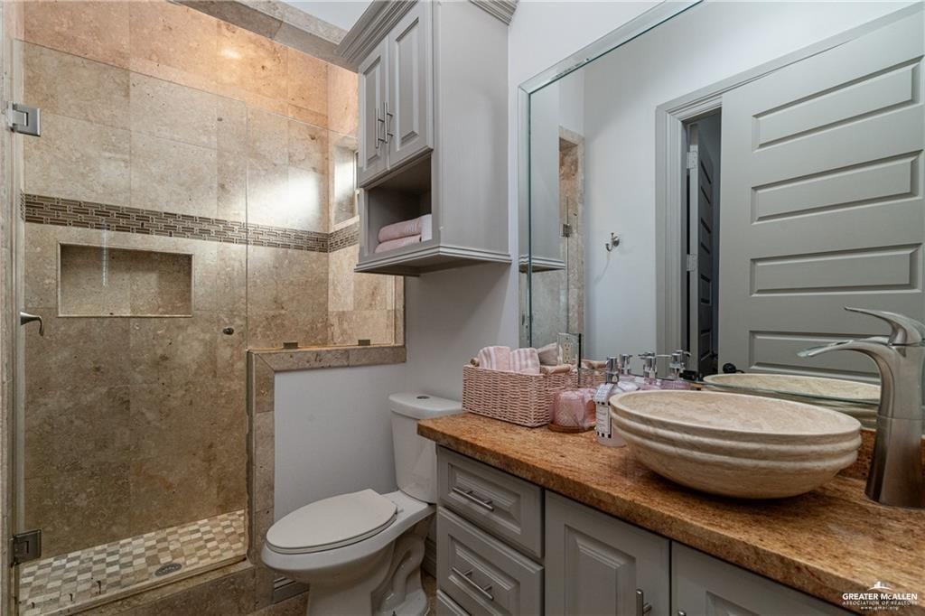 1205 Travis Street Mission, TX 78572 - Photo 21 of 45 a bathroom with a granite countertop sink a toilet and a mirror