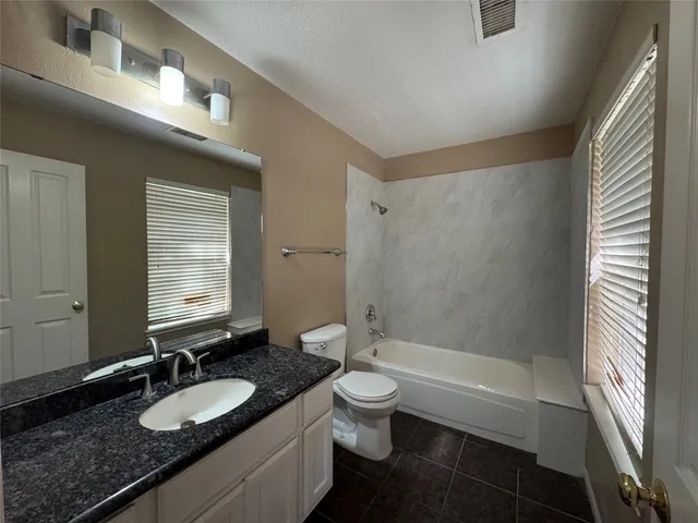 a bathroom with a granite countertop sink a toilet a mirror and shower