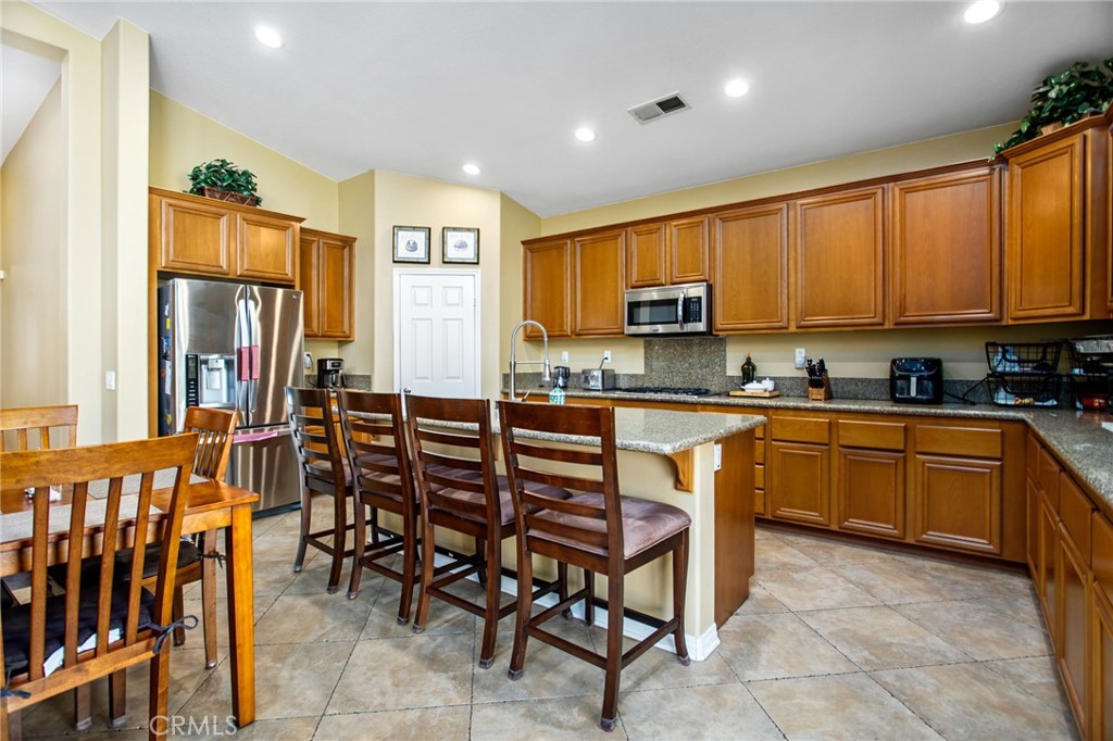 31677 Middlebrook Lane Menifee, CA 92584 - Photo 14 of 42 a kitchen with stainless steel appliances granite countertop a stove a sink a refrigerator with a dining table and chairs