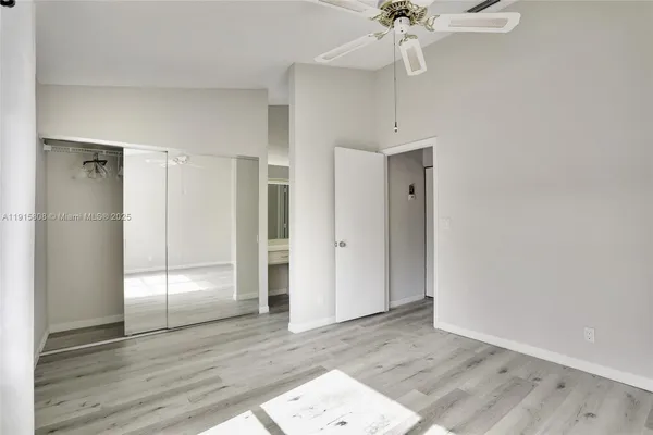 a view of an empty room with wooden floor and a ceiling fan