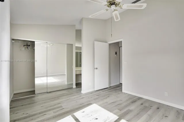 a view of an empty room with wooden floor and a ceiling fan