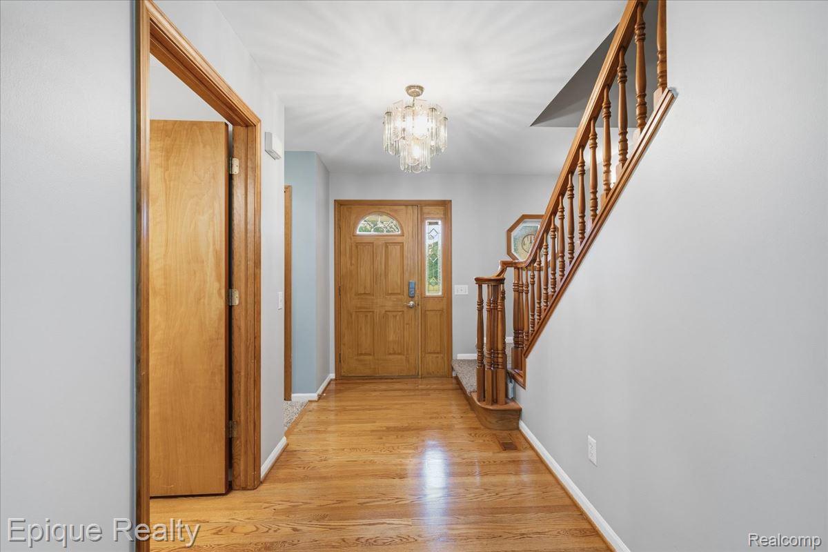 1221 Rhodes Road Lake Orion, MI 48360 - Photo 10 of 72 Foyer featuring wood-finish flooring, a solid wood entry door with decorative glass, an ornate chandelier, and a wood staircase with balusters