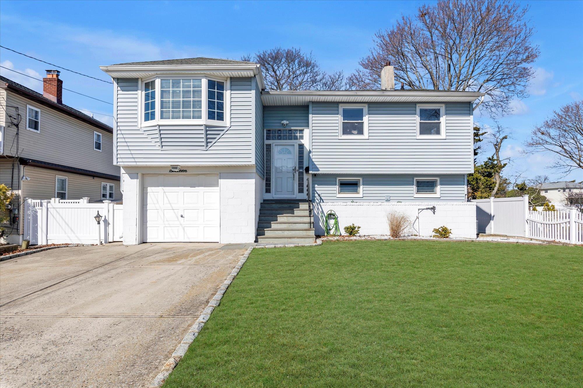 Bi-level home with driveway, a garage, fence, and a front lawn