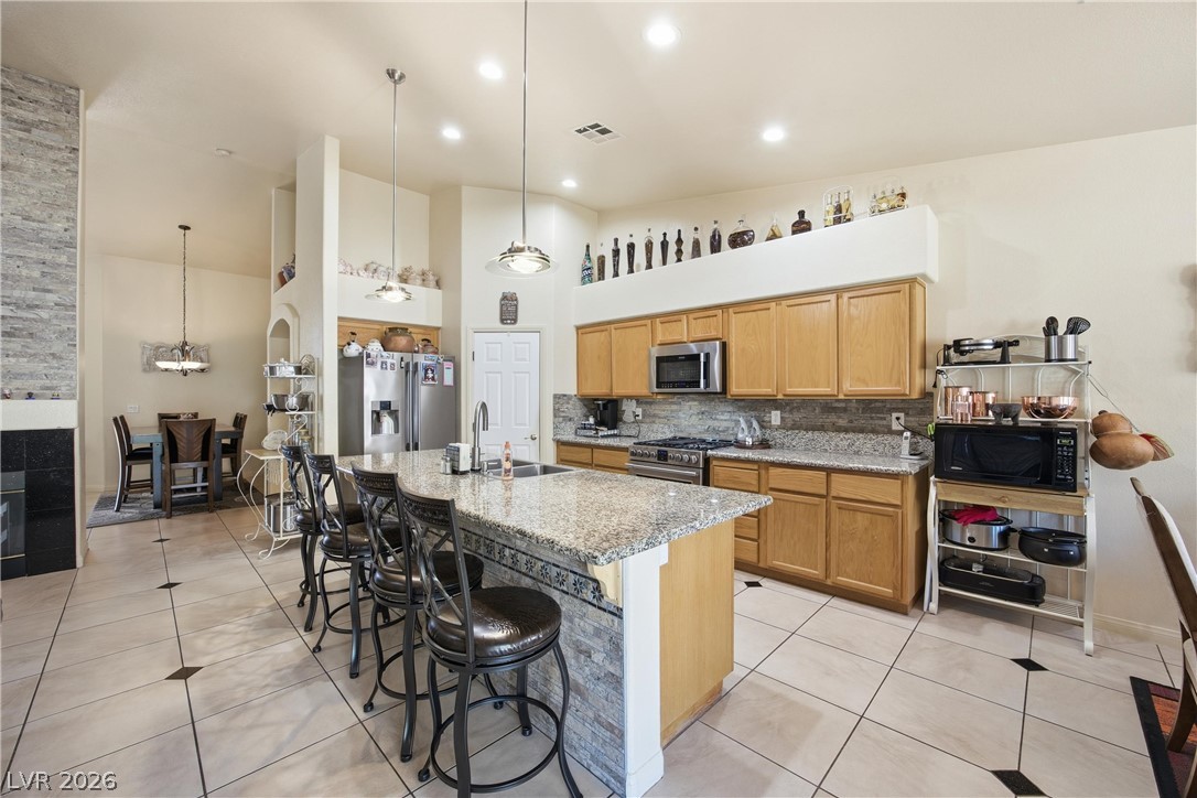 6109 Ocho Rios Street Las Vegas, NV 89130 - Photo 10 of 36 Kitchen with light tile patterned flooring, a high ceiling, stainless steel appliances, hanging light fixtures, and a center island with sink