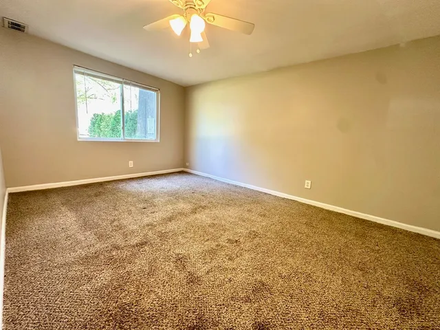 an empty room with a chandelier fan and windows