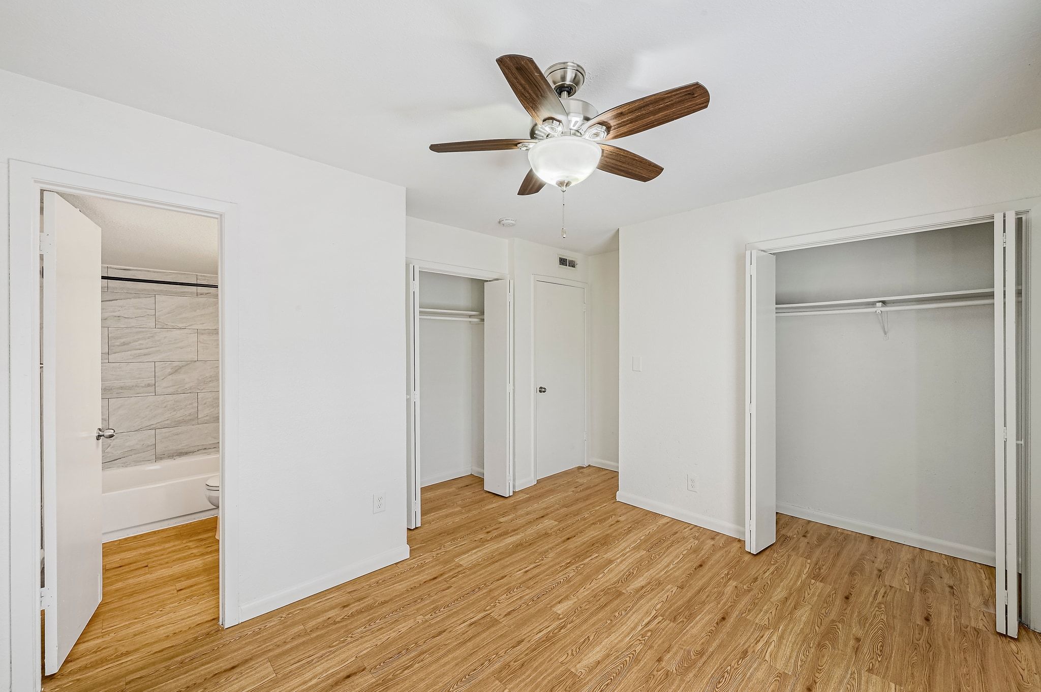 2207 Leon Street, Unit 201 Austin, TX 78705 - Photo 13 of 19 Unfurnished bedroom featuring two closets, light wood finished floors, ceiling fan, and ensuite bath