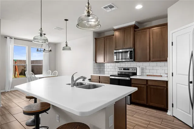 a kitchen with kitchen island a sink stainless steel appliances and chairs