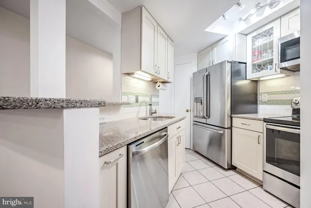 a kitchen with stainless steel appliances granite countertop a refrigerator a sink and white cabinets