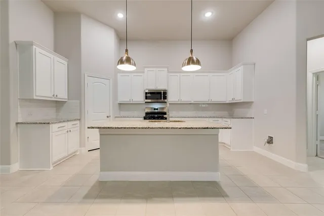 a kitchen with kitchen island granite countertop a stove a sink a refrigerator and white cabinets with wooden floor
