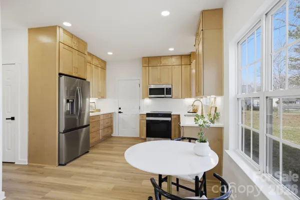 a kitchen with stainless steel appliances granite countertop a refrigerator a stove a sink dishwasher a dining table and chairs with wooden floor