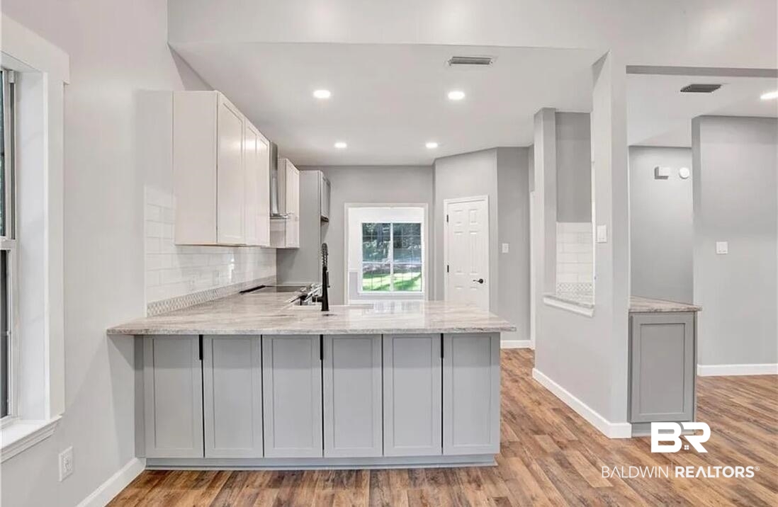 632 Ridgewood Drive Daphne, AL 36526 - Photo 14 of 36 Kitchen featuring gray cabinets, kitchen peninsula, backsplash, light hardwood / wood-style floors, and light stone counters