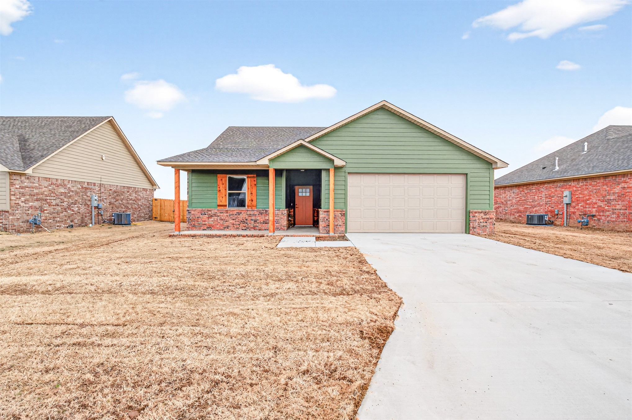 124 Countryside Way Pocola, OK 74902 - Photo 2 of 39 Single-story residence featuring green siding, brick accents, a covered front porch, and an attached garage with a concrete driveway