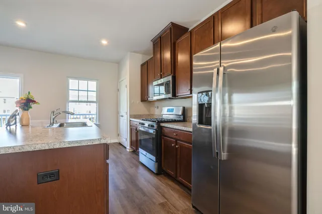 a kitchen with stainless steel appliances granite countertop a refrigerator a stove and a sink with wooden floor