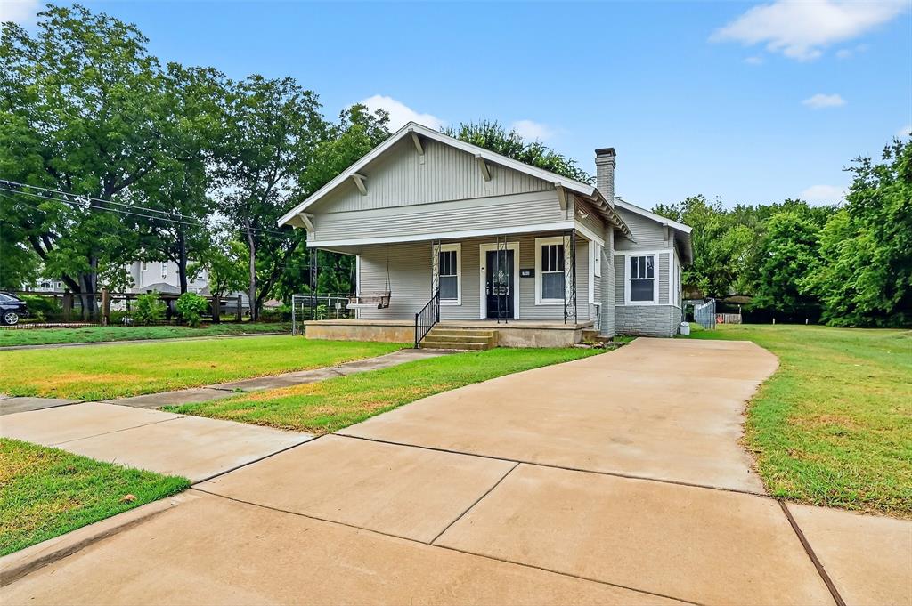 Bungalow-style house featuring a porch, a front lawn, a chimney, and driveway