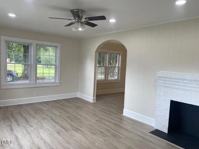 an empty room with wooden floor a ceiling fan a fireplace and windows