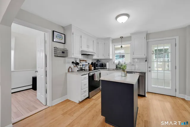 a kitchen with stainless steel appliances granite countertop a refrigerator a sink dishwasher and white cabinets with wooden floor