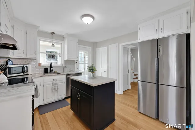 a kitchen with stainless steel appliances granite countertop a refrigerator a sink dishwasher a stove and white cabinets with wooden floor