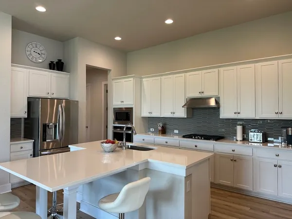 a kitchen with stainless steel appliances a sink a stove a refrigerator cabinets and chairs