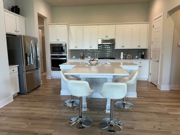 a kitchen with stainless steel appliances a dining table chairs refrigerator and sink