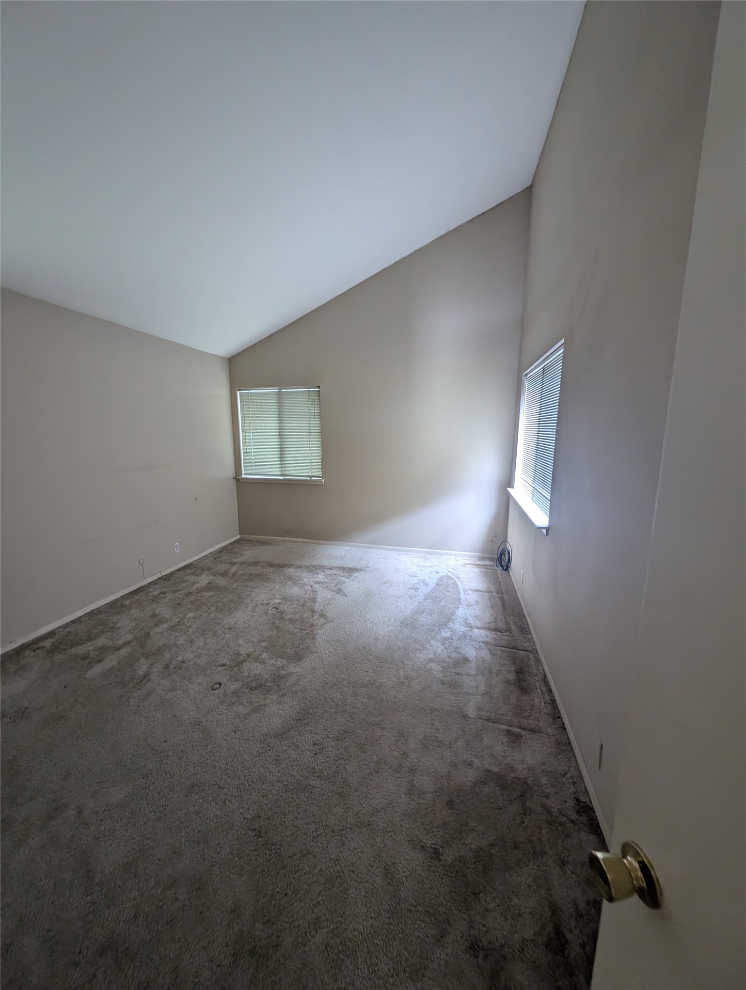 1653 Prairie Mark Lane Houston, TX 77077 - Photo 19 of 24 Room features a high, sloped ceiling with two windows providing natural light. The carpeted floor and neutral wall color offer a versatile space for various design ideas.