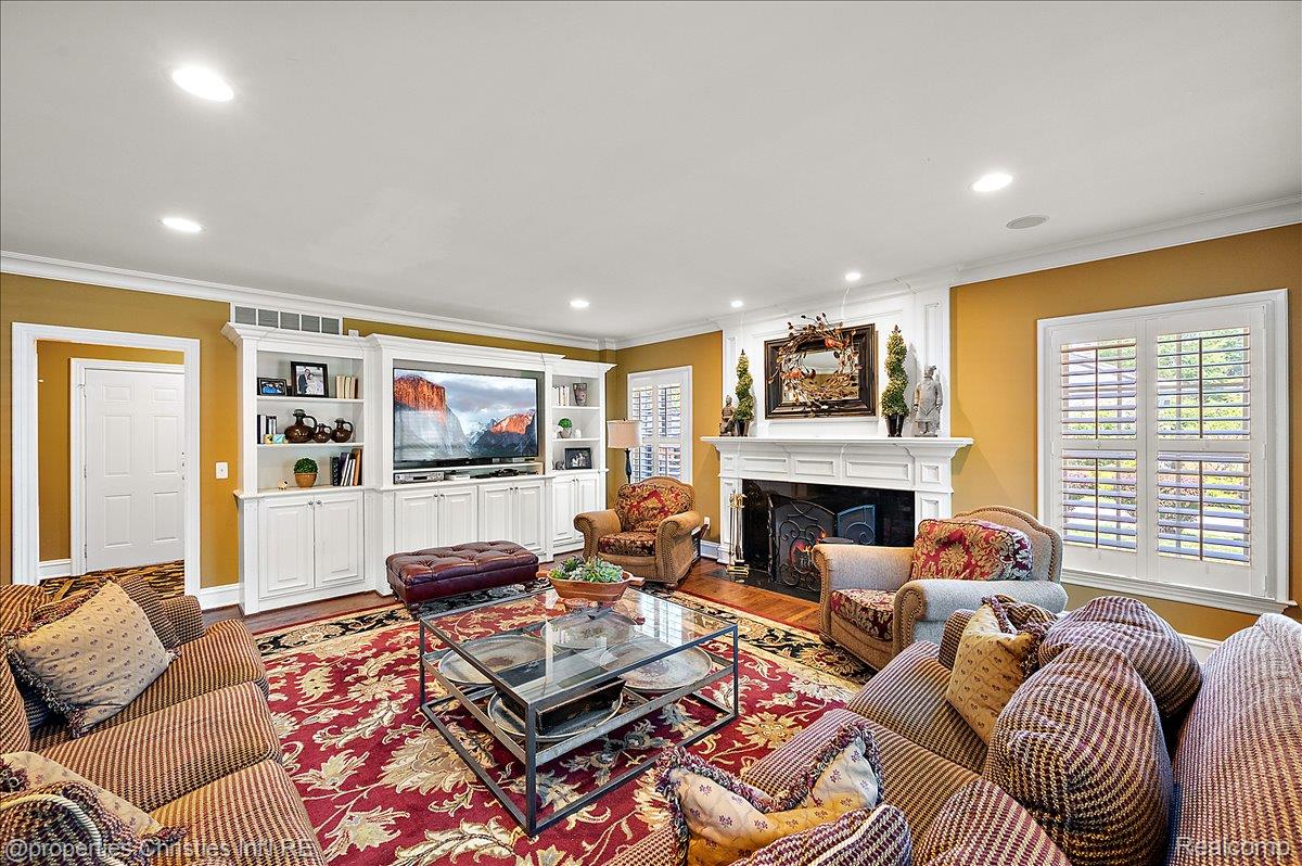 135 Clifton Road Bloomfield Hills, MI 48301 - Photo 27 of 77 Living room featuring a prominent fireplace with a detailed white mantelpiece, built-in white cabinetry, wood-finish flooring, and recessed ceiling lighting