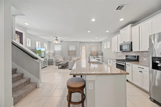 a kitchen with stainless steel appliances granite countertop a sink dishwasher a refrigerator and white cabinets with wooden floor