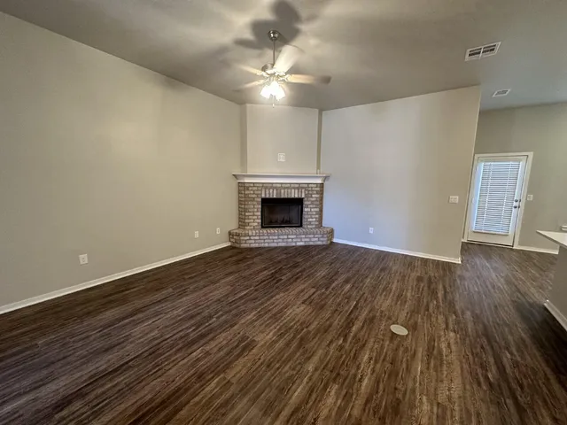 a view of an empty room with wooden floor fireplace and a window
