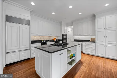a kitchen with granite countertop a white stove top oven and white cabinets with wooden floor