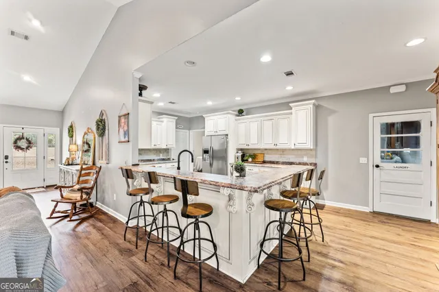 a kitchen with stainless steel appliances kitchen island granite countertop a stove top oven a sink a dining table and chairs with wooden floor