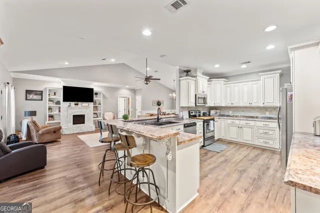 a kitchen with stainless steel appliances granite countertop a stove top oven a sink dishwasher and white cabinets with wooden floor