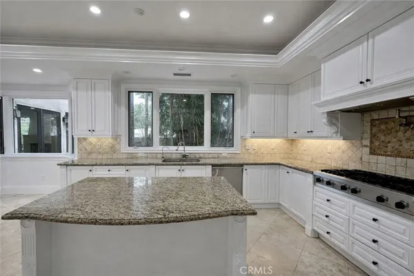 a large kitchen with granite countertop a sink and white cabinets