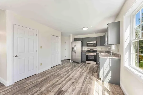 a kitchen with granite countertop a refrigerator oven a sink dishwasher and white cabinets with wooden floor