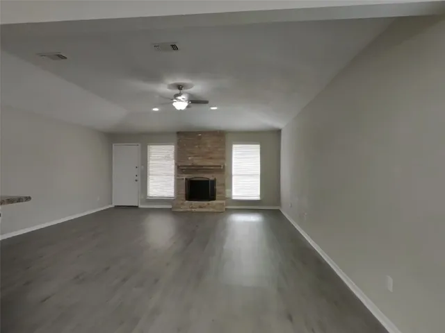an empty room with wooden floor fireplace and windows