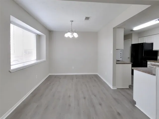 an empty room with wooden floor a chandelier fan and windows