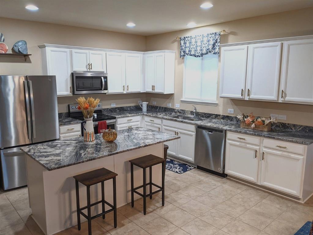 2213 Heaton Street Forney, TX 75126 - Photo 6 of 14 Kitchen featuring a central island with a stone countertop, white cabinetry with bronze-finish hardware, stainless steel appliances, and recessed lighting