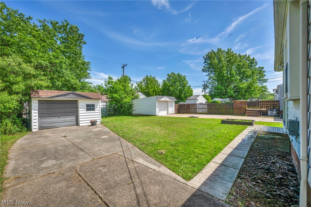 4117 Wyncote Road South Euclid, OH 44121 - Photo 49 of 50 Expansive backyard featuring a concrete driveway, detached garage with dark gray door, manicured lawn, and a secondary storage shed