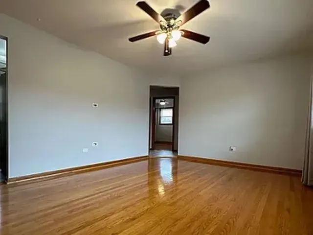 a view of an empty room with wooden floor and a ceiling fan