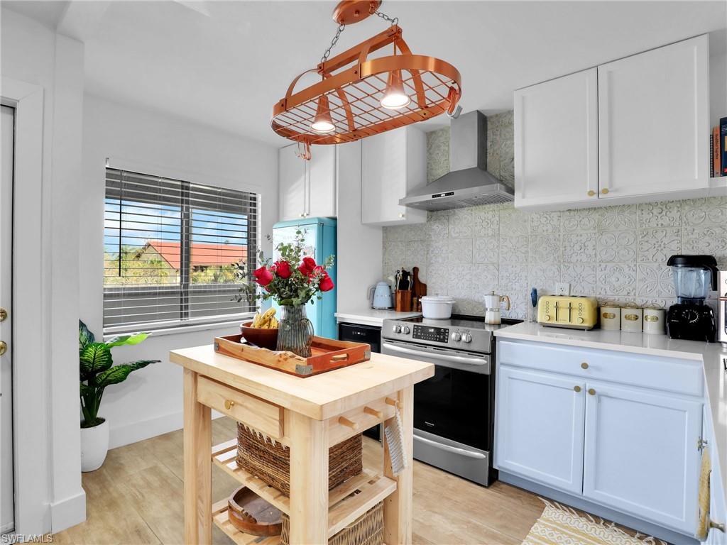 9831 Alabama Street, Unit 5 Bonita Springs, FL 34135 - Photo 6 of 28 Kitchen with electric range, wall chimney range hood, decorative backsplash, white cabinets, and freestanding refrigerator